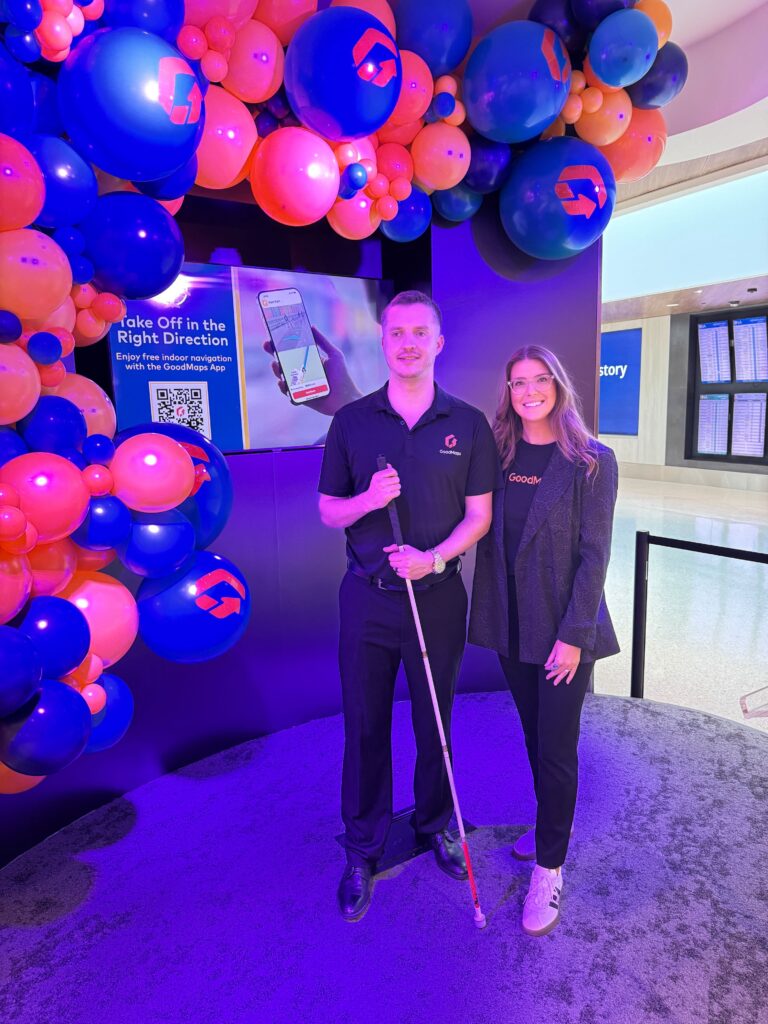 Kevin and Evelyn stand on a stage lit in blue and red, surrounded by balloons featuring the GoodMaps and BNA logos.