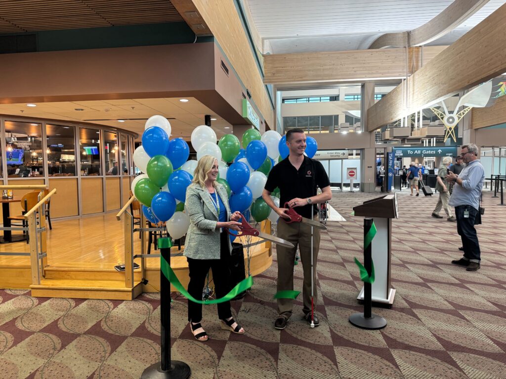 Kevin holds a pair of large scissors and cuts the ribbon, officially launching GoodMaps at EUG Airport.