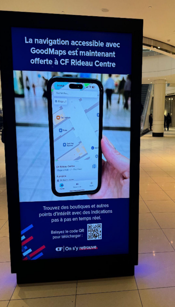 Digital mall kiosk at CF Rideau Centre displaying a French-language ad for GoodMaps accessible navigation, showing a smartphone with an indoor map and a QR code to download the app.