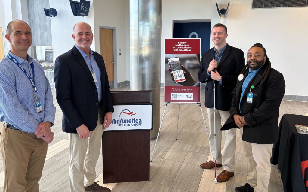 Four people standing in the MidAmerica St. Louis Airport terminal next to a podium and a GoodMaps promotional sign, posing for a photo at an indoor event.