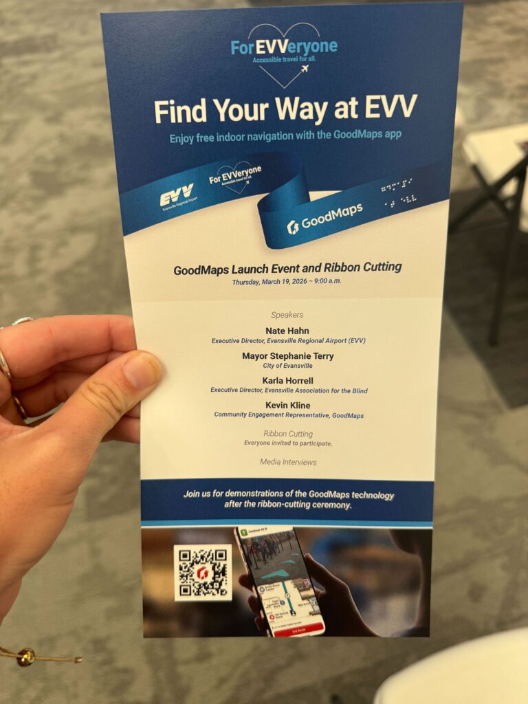 A hand holds a GoodMaps ‘Find Your Way at EVV’ launch event flyer listing speakers and event details, with a QR code and navigation app image at the bottom.
